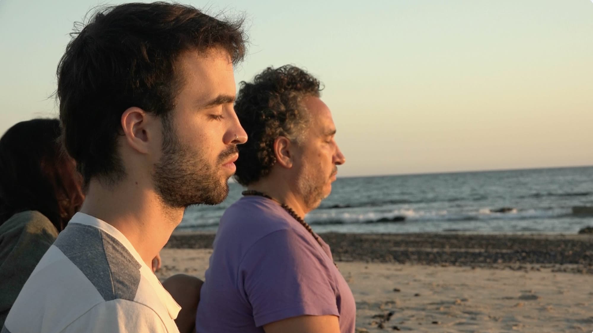 Dois participantes do retiro de olhos fechados de frente para o mar, ao entardecer