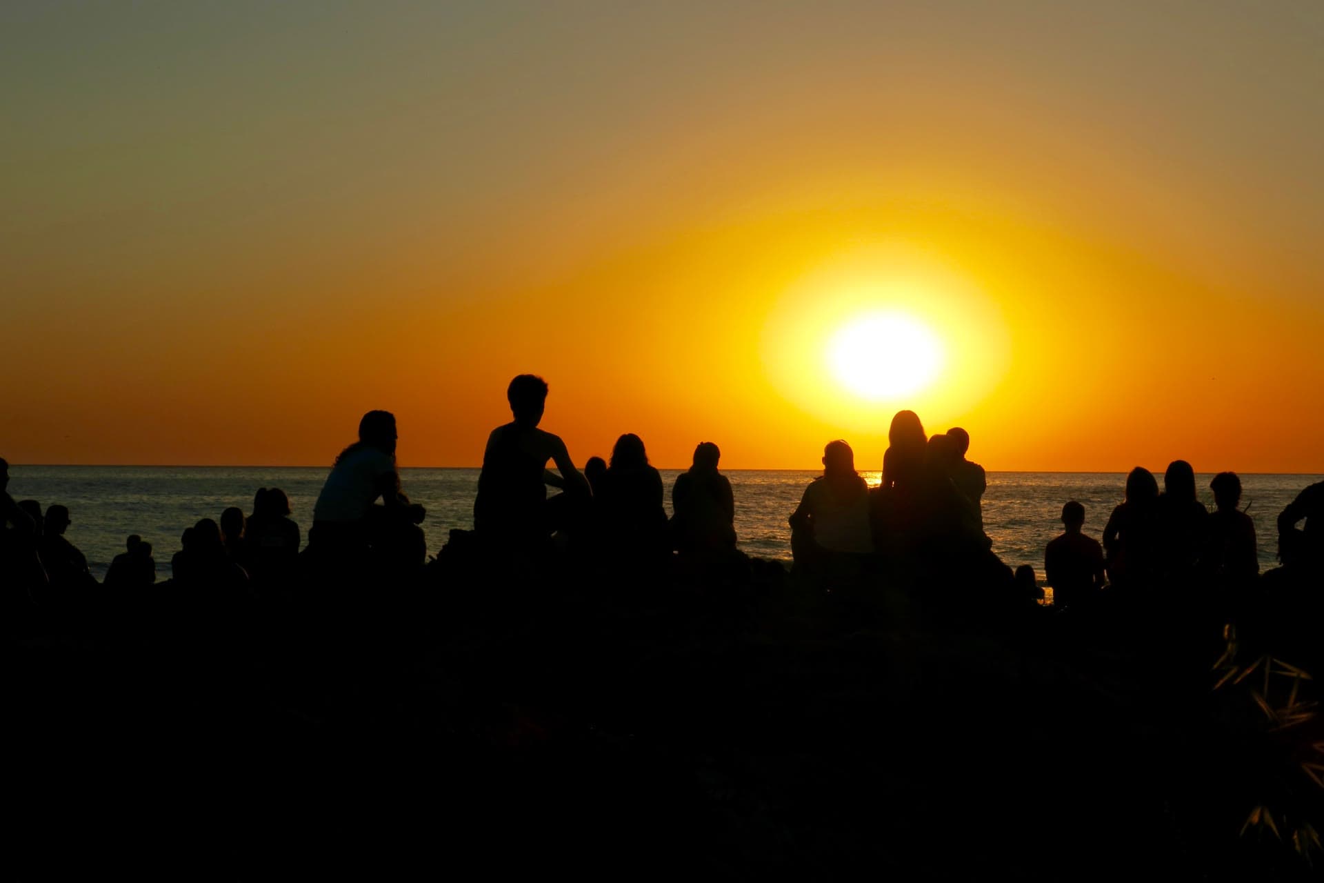 Grupo del retiro sentado frente al mar al atardecer, a contraluz del sol